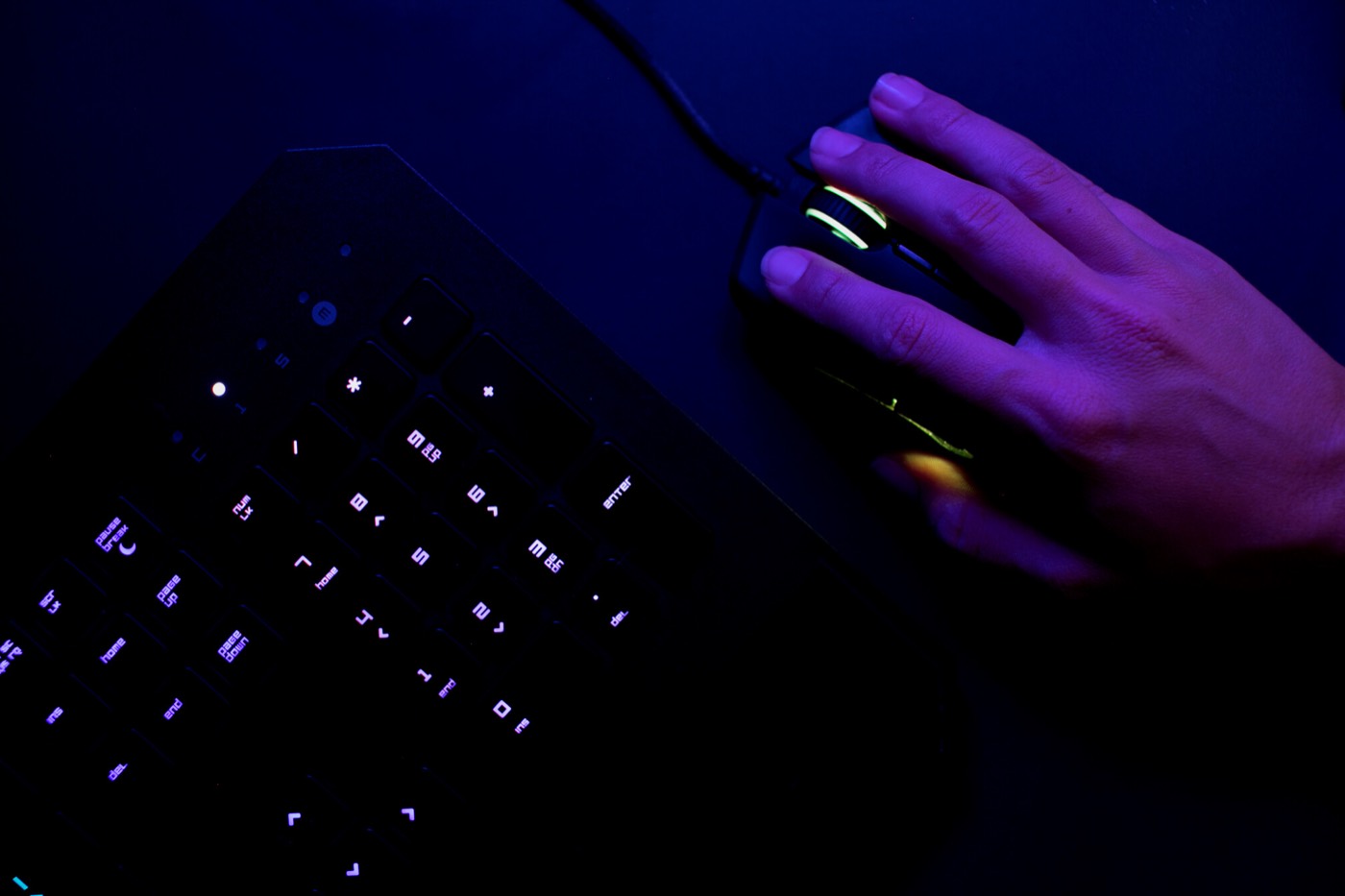 Mano usando un mouse junto a un teclado retroiluminado
